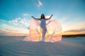 A girl in a fly white dress dances and poses in the sand desert at sunset Royalty Free Stock Photo