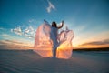 A girl in a fly white dress dances and poses in the sand desert at sunset Royalty Free Stock Photo