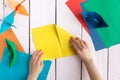 A girl folds colored paper to make origami. A girl makes origami on a wooden table