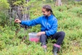 A positive pretty girl in a forest area collects ripe healthy tasty lingonberries in a plastic bucket.