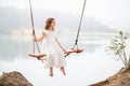 A girl in the forest swinging on a swing. Rope swing on a forest lake. Barefoot girl in a white dress with long hair Royalty Free Stock Photo