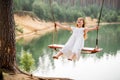 A girl in the forest swinging on a swing. Rope swing on a forest lake. Barefoot girl in a white dress with long hair Royalty Free Stock Photo