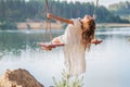 A girl in the forest swinging on a swing. Rope swing on a forest lake. Barefoot girl in a white dress with long hair Royalty Free Stock Photo