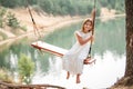 A girl in the forest swinging on a swing. Rope swing on a forest lake. Barefoot girl in a white dress with long hair Royalty Free Stock Photo