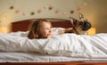 A girl and a Bulldog puppy lie on the bed under the covers and look towards the window. Friendship and pet care. Royalty Free Stock Photo