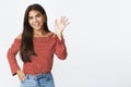 Girl friendly waving with raised hand and saying hello, smiling broadly at camera getting know new people, greeting and