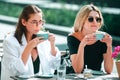 Girl friends in cafe outdoor. Two beautiful girls with cups coffee in summer cafe. Outdoors portrait of two young Royalty Free Stock Photo