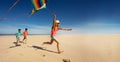 Girl and friends run fast on beach hold color kite Royalty Free Stock Photo