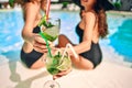 Girl friends in swimming-pool with cocktails