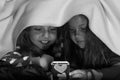 Girl friends under blanket playing with mobile phone