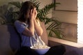 Girl with a frightening face is watching TV and covered her face with her hands.