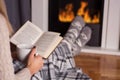 Girl in front of the fireplace reading book and warming feet on fire Royalty Free Stock Photo