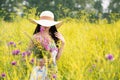 A girl with a full basket of flowers in a light long summer dress stands in the middle of a yellow flower field. Royalty Free Stock Photo