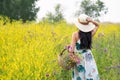 A girl with a full basket of flowers in a light long summer dress stands in the middle of a yellow flower field. Royalty Free Stock Photo