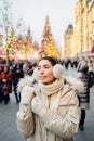 Girl in fur hood headphones in Christmas market decorated with holiday lights in the evening. Christmas tree lights on background