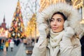 Girl in fur hood walking in Christmas market decorated with holiday lights in the evening. Christmas tree lights on background.