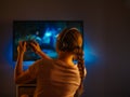 Girl gamer in headphones and a joystick in her hands plays a video game. Neon light. Night. Shooting from the back. Entertainment