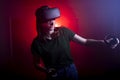 Girl gamer in modern wireless virtual reality glasses plays a shooter on a dark red-blue background, a woman shoots with game Royalty Free Stock Photo