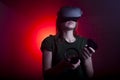 Girl gamer in modern virtual reality glasses plays a shooter on a dark red-blue background, a woman shoots with game joysticks Royalty Free Stock Photo