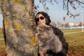 A girl with glasses and a knitted hat helps the cat climb a tree Royalty Free Stock Photo