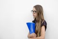 Girl with glasses with long hair standing against the wall and holding a blue folder Royalty Free Stock Photo