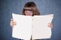 Girl in glasses looking over newspaper