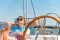 A girl in glasses sits near the wheel next to on the deck of a yacht looking around. Royalty Free Stock Photo