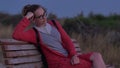 Girl in glasses sitting on bench watching the evening sea