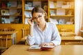 Girl with glasses sitting at a table with a book in the classroom, holding a pencil in his hand, thoughtful look Royalty Free Stock Photo