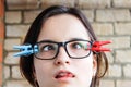 A girl with glasses with slanted eyes and clothespins attached to her glasses. Humor, absurdity