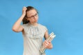 A girl in glasses and with textbooks in her hand is scratching her head with her hand Royalty Free Stock Photo