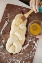 Girl glazing plaited challah dough with mum, overhead close up