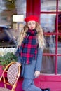 Girl in a gray coat and a red beret with curls stands thoughtfully near a cafe on a background of a red facade Royalty Free Stock Photo