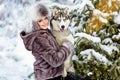 The girl in the gray coat smiling next to a grey husky dog in wi Royalty Free Stock Photo