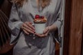 Girl in gray robe holds white cup of tea or coffee and Belgian waffle with berries on the porch of the house in summer Royalty Free Stock Photo