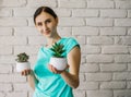 A girl in a green blouse holds a houseplant. A young woman on a white brick background with a small pot of office plant