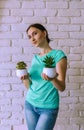 A girl in a green blouse holds a houseplant. A young woman on a white brick background with a small pot of office plant