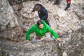 Girl in a green coat climbing cliffs on the background of other climbers