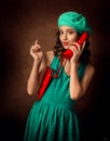 A girl in a green dress and a green beret is talking on a red phone. The girl is flirting. Pin Up.