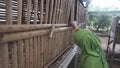 A girl in a green hijab feeds a rabbit in a traditional bamboo wooden hutch, fostering a heartwarming