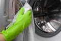 Girl in green protective gloves wipes door washing machine dryly with napkin Royalty Free Stock Photo