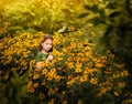 A girl in a green sweater sits in a flower bed of yellow flowers, doronicum.