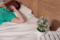 A girl in a green T-shirt and blue jeans is sleeping on the bed with a book covering her face, next to a flower on a chair Royalty Free Stock Photo