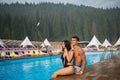 Girl and guy sitting on the edge of swimming pool at the resort and making selfie photo on the phone with selfie stick Royalty Free Stock Photo