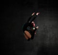 Girl gymnast in black sport body and uppers jumping and making dymnastic pose in air over dark background