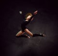 Girl gymnast in black sport body and uppers jumping and making dymnastic pose in air over dark background