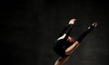 Girl gymnast in black sport body and uppers jumping and making dymnastic pose in air over dark background