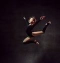 Girl gymnast in black sport body and uppers jumping and making dymnastic pose in air over dark background