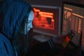 Girl hacker in the hood holding the phone in hands trying to hack the mobile device cloud in the dark under neon light Royalty Free Stock Photo