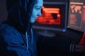 Girl hacker in a hood typing program code while committing a cybercrime hacking a system on the background of screens